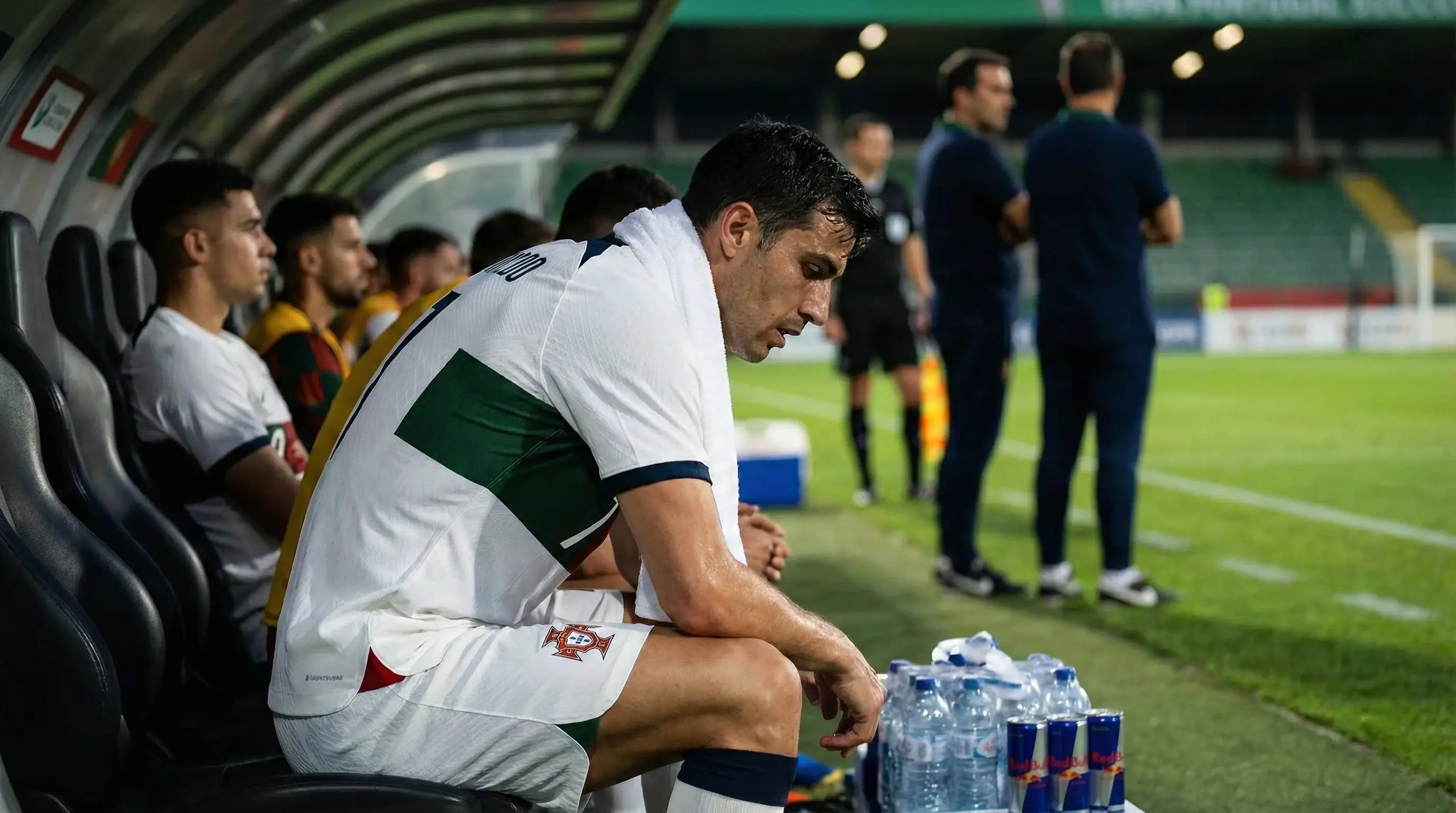 Jogador de futebol sentado no banco a descansar durante o intervalo do jogo mostrando sinais de cansaço